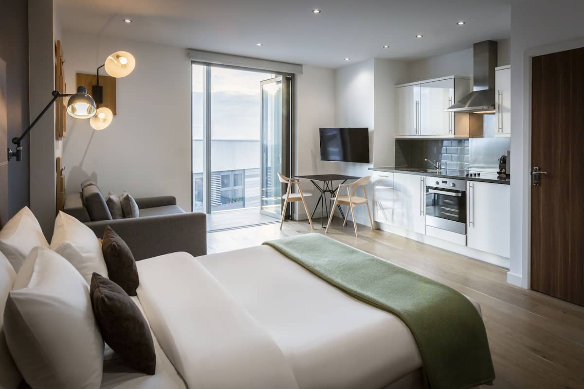 Une chambre d’hôtel moderne dotée d’un grand lit, d’un balcon avec vue, d’une kitchenette et d’un téléviseur à écran plat.