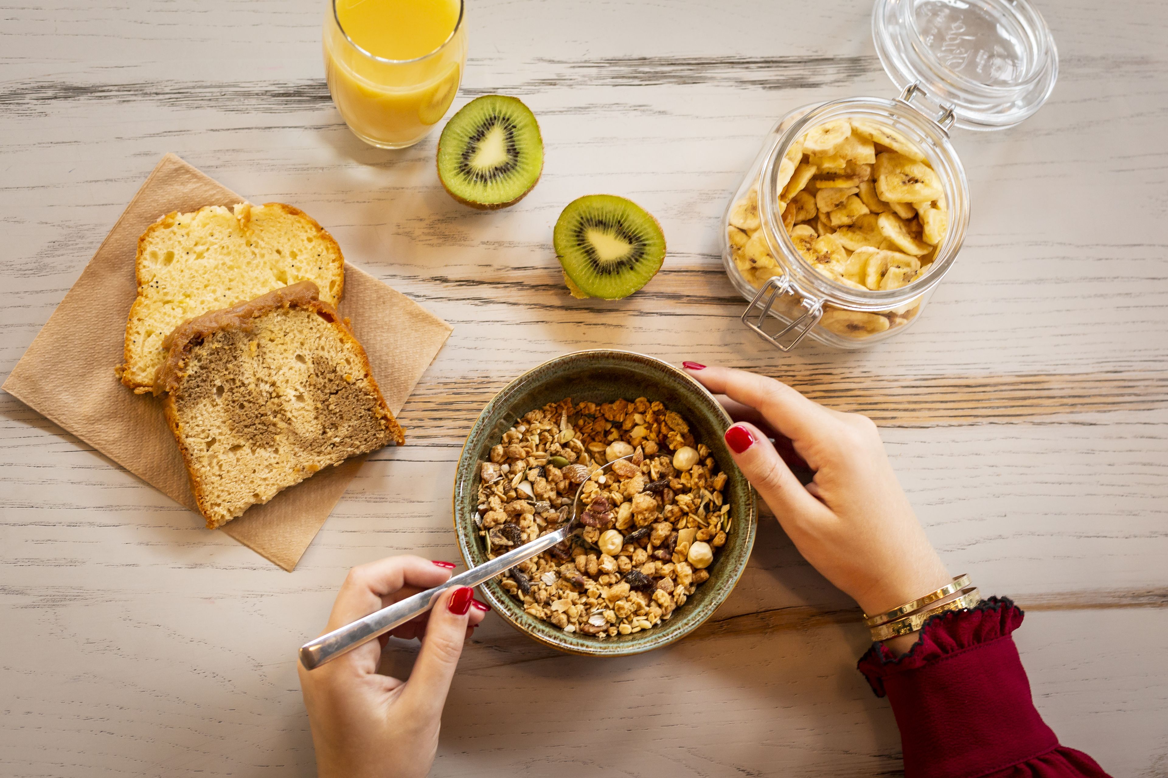A breakfast setting with bread, kiwi, granola, and a glass of orange juice on a wooden table.
