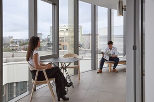 Un espacio de oficina moderno con ventanas amplias, una mesa y dos personas conversando.