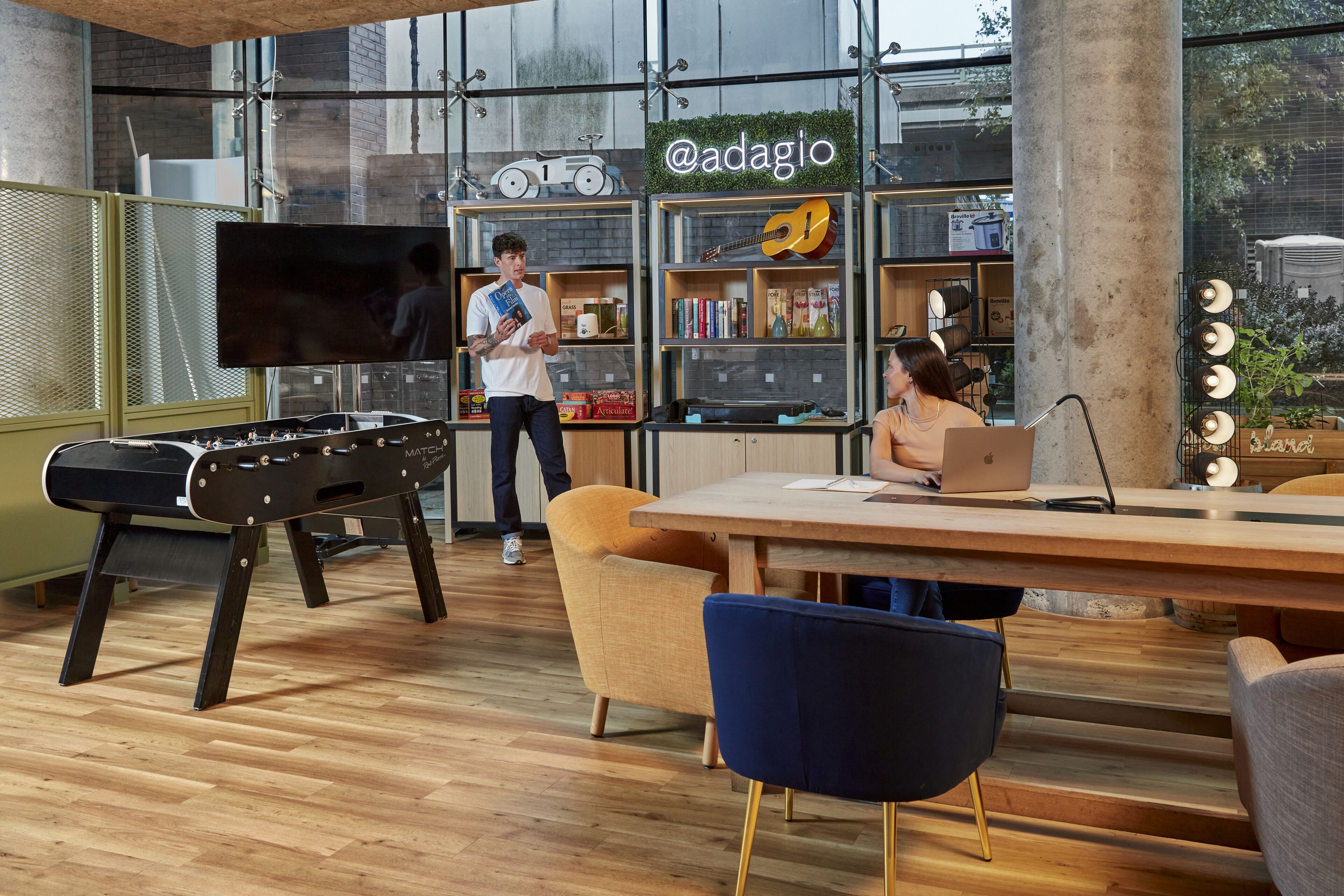 A modern indoor space with a pool table, a large TV, and a sign reading "@adagio".
