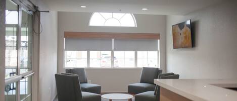 A reception area with two armchairs, a round table, a reception desk, and a large window with a view of parked cars.