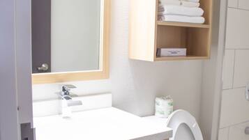 A bathroom with a white sink, a mirror, a wooden shelf with towels, and a toilet.