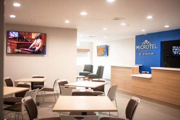 A hotel lobby with a reception desk, seating area, and a television displaying a courtroom scene.
