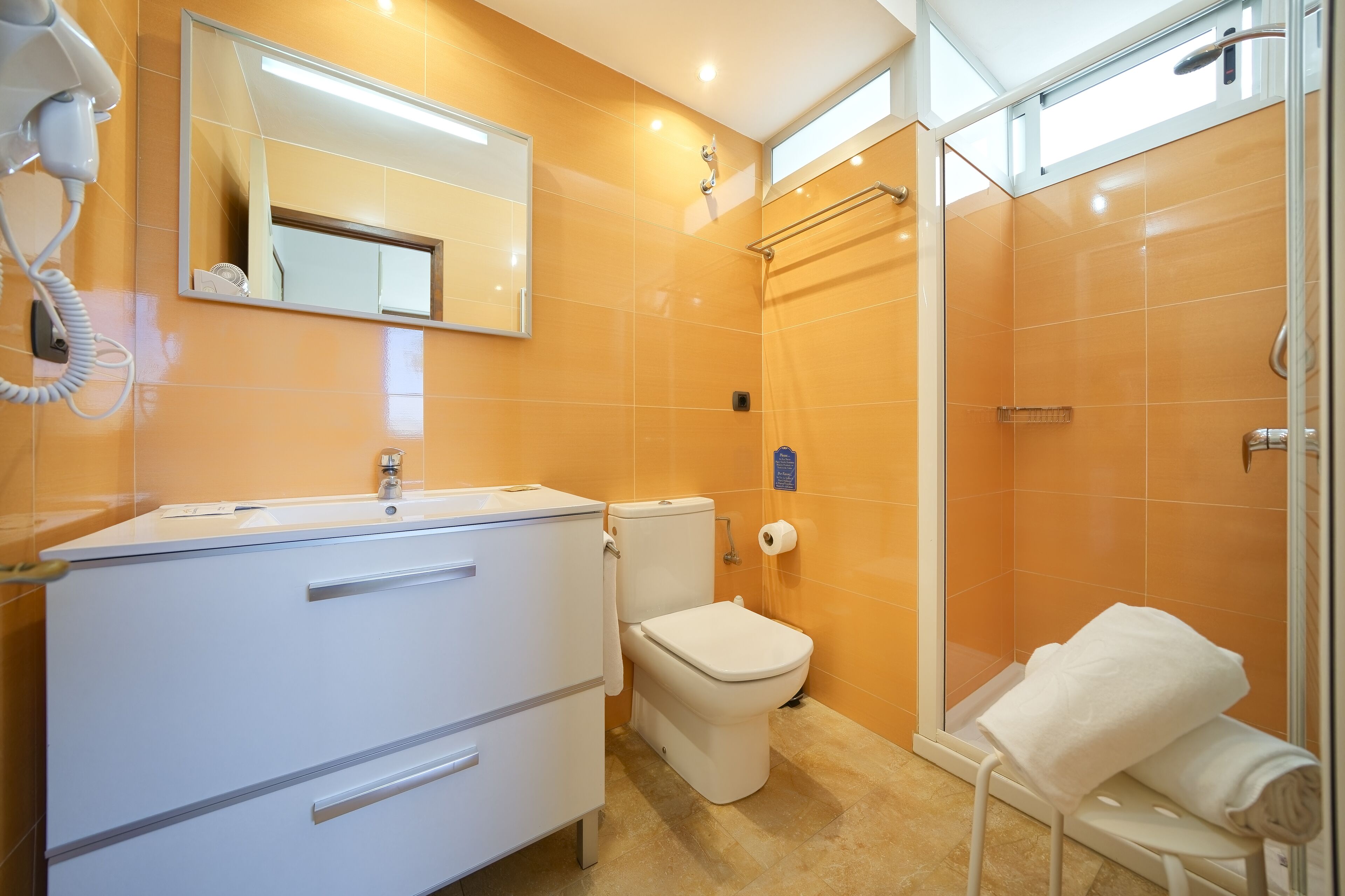 A modern bathroom with a white vanity, a toilet, a shower area, and a towel rack.