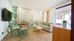 Una sala de estar con un sofá, una butaca color turquesa, dos mesitas y un televisor montado en la pared.