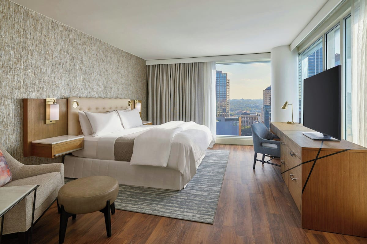 A modern hotel room with a large bed, a desk, a chair, and a TV.