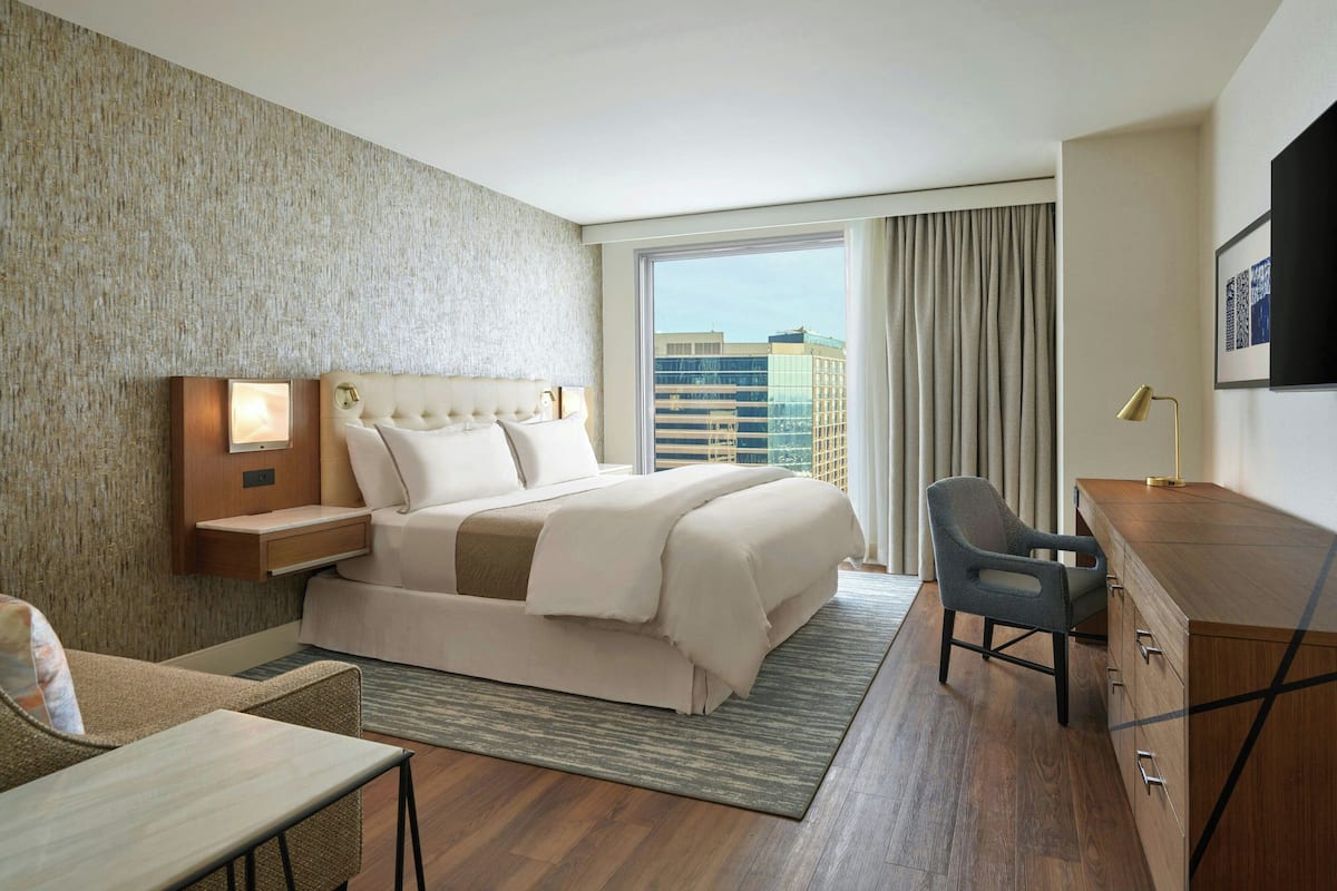 A hotel room with a large bed, a desk, a chair, and a view of the city.