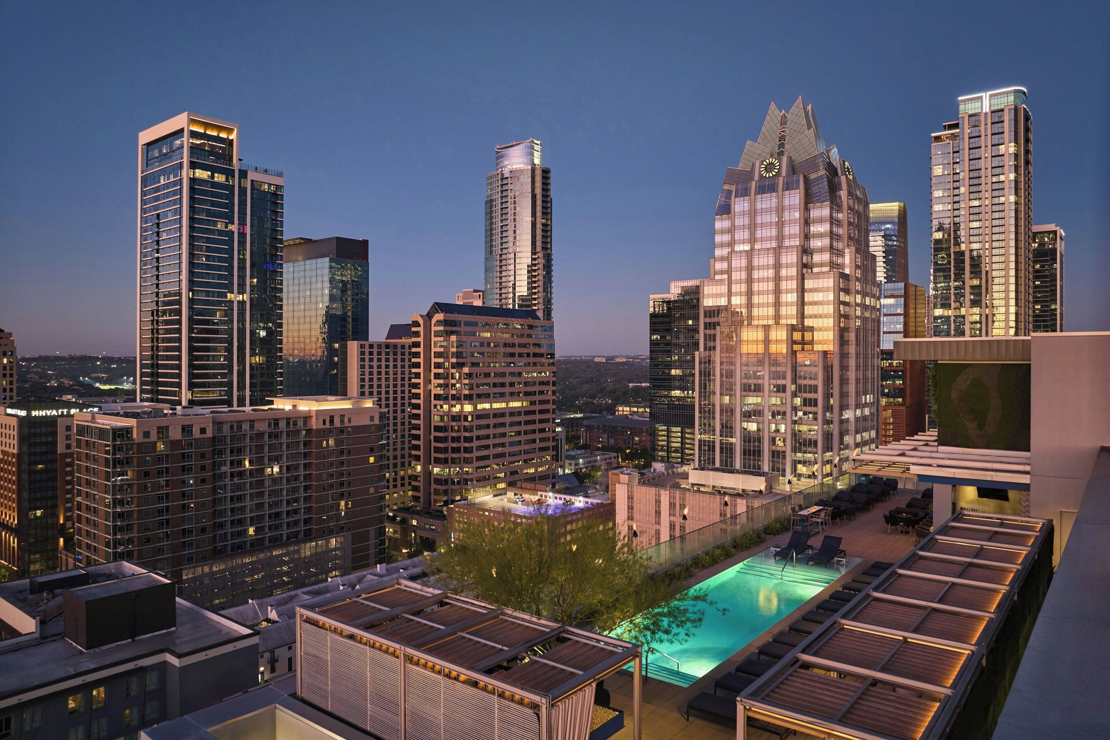 A cityscape with modern high-rise buildings, a rooftop pool area with lounge chairs, and a view of the city.