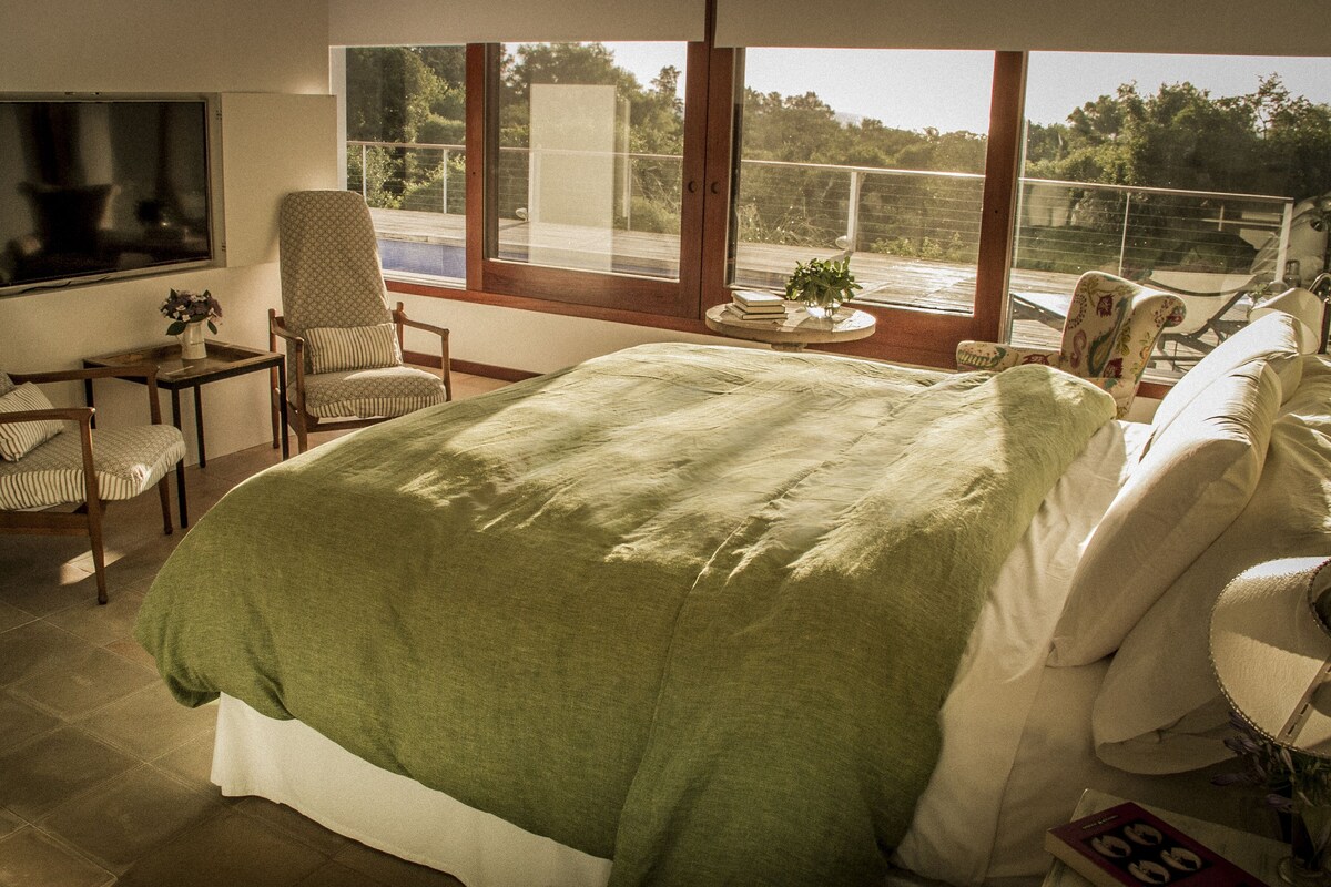 A bedroom with a large bed, two chairs, a small table, and a TV.