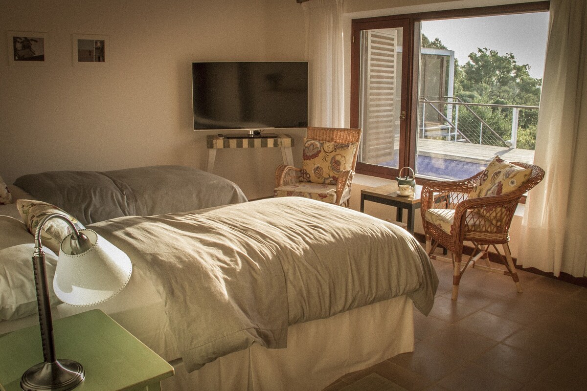 A hotel room with two beds, a television, a table, and a balcony with a pool.