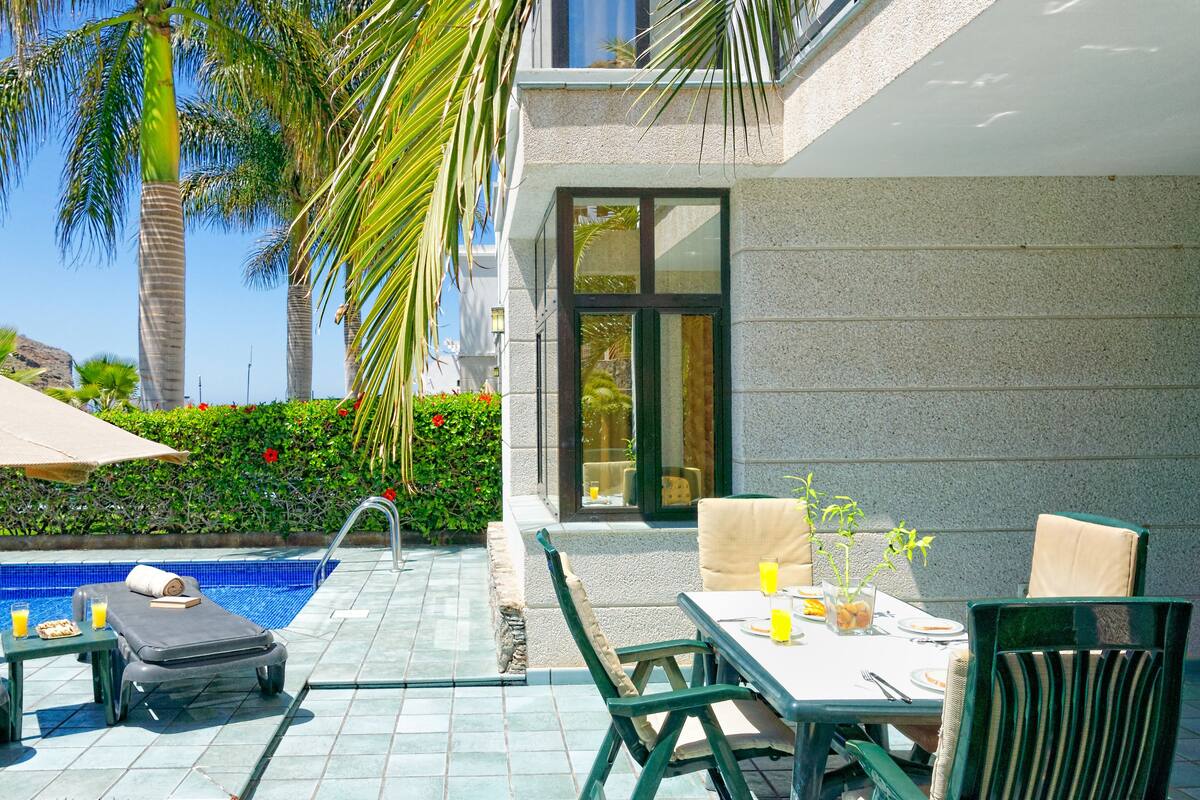 A poolside area with lounge chairs, a table with breakfast items, and a view of a building with a stone facade.