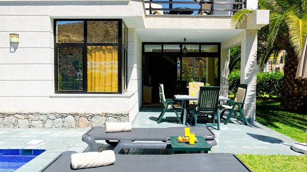 Een modern overdekt terras met een zwembad, lounge stoelen en een eethoek.