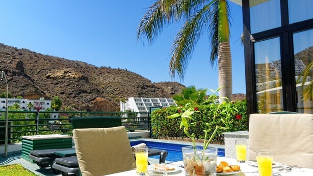 Un coin repas avec une table mise pour le petit-déjeuner, donnant sur une piscine et un paysage montagneux.
