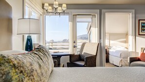 A hotel room with a bed, a chair, a desk, and a view of the ocean.