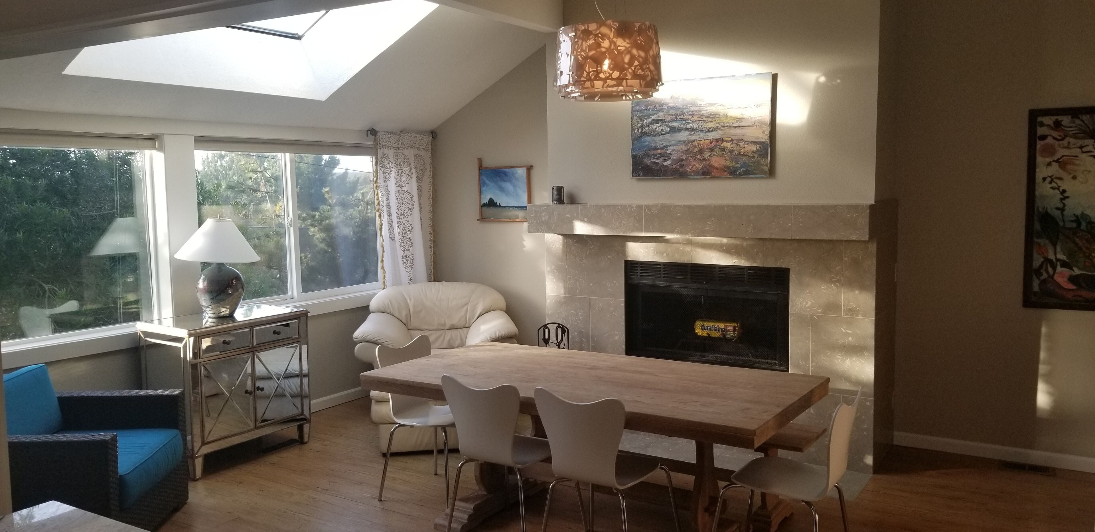 Un comedor con mesa y sillas de madera, chimenea y vistas a la vegetación por la ventana.