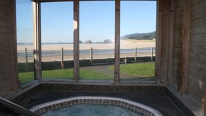 A wooden cabin with a hot tub and a view of a beach.