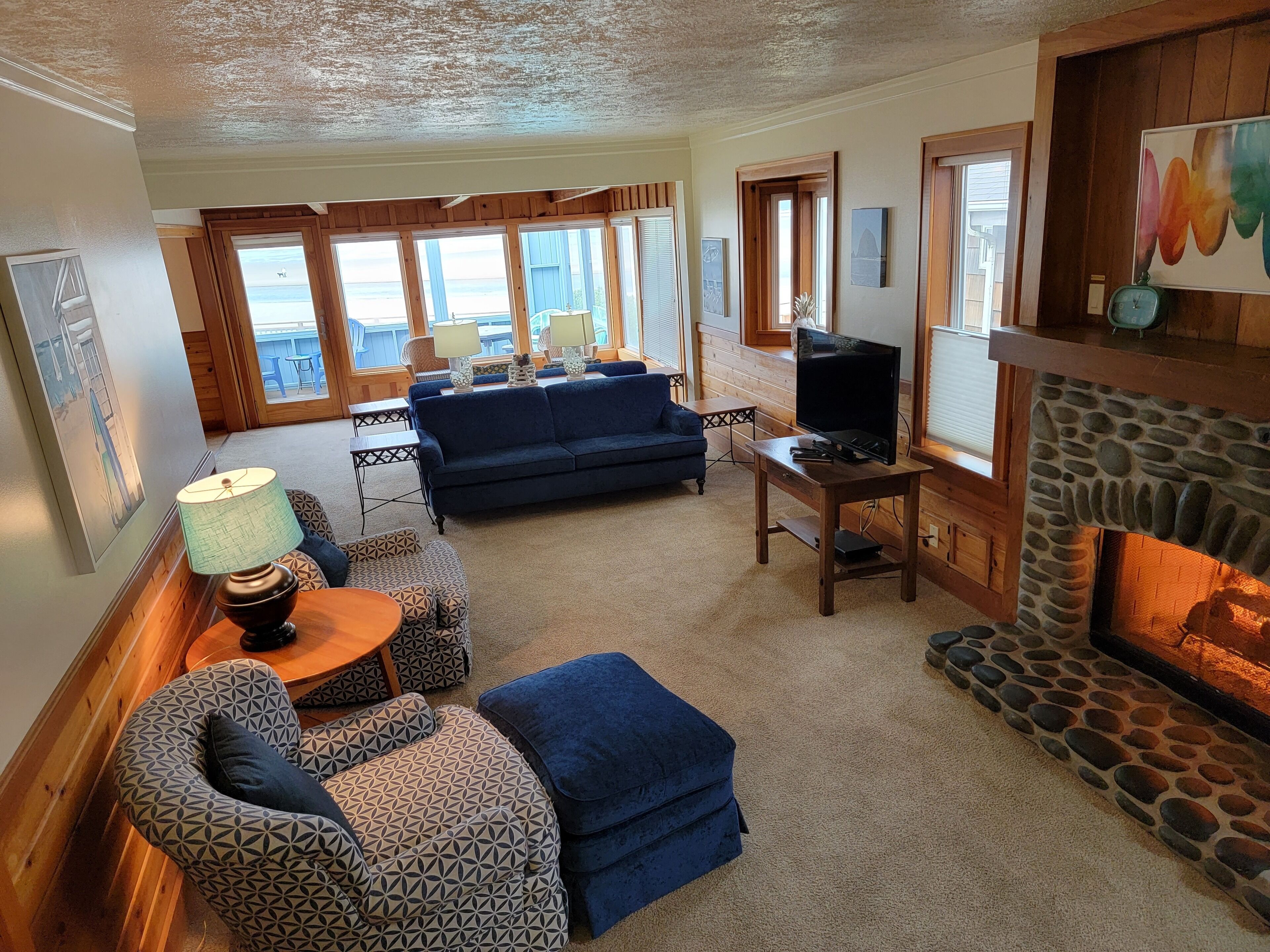 A cozy living room with a blue sofa, patterned ottoman, and a stone fireplace.