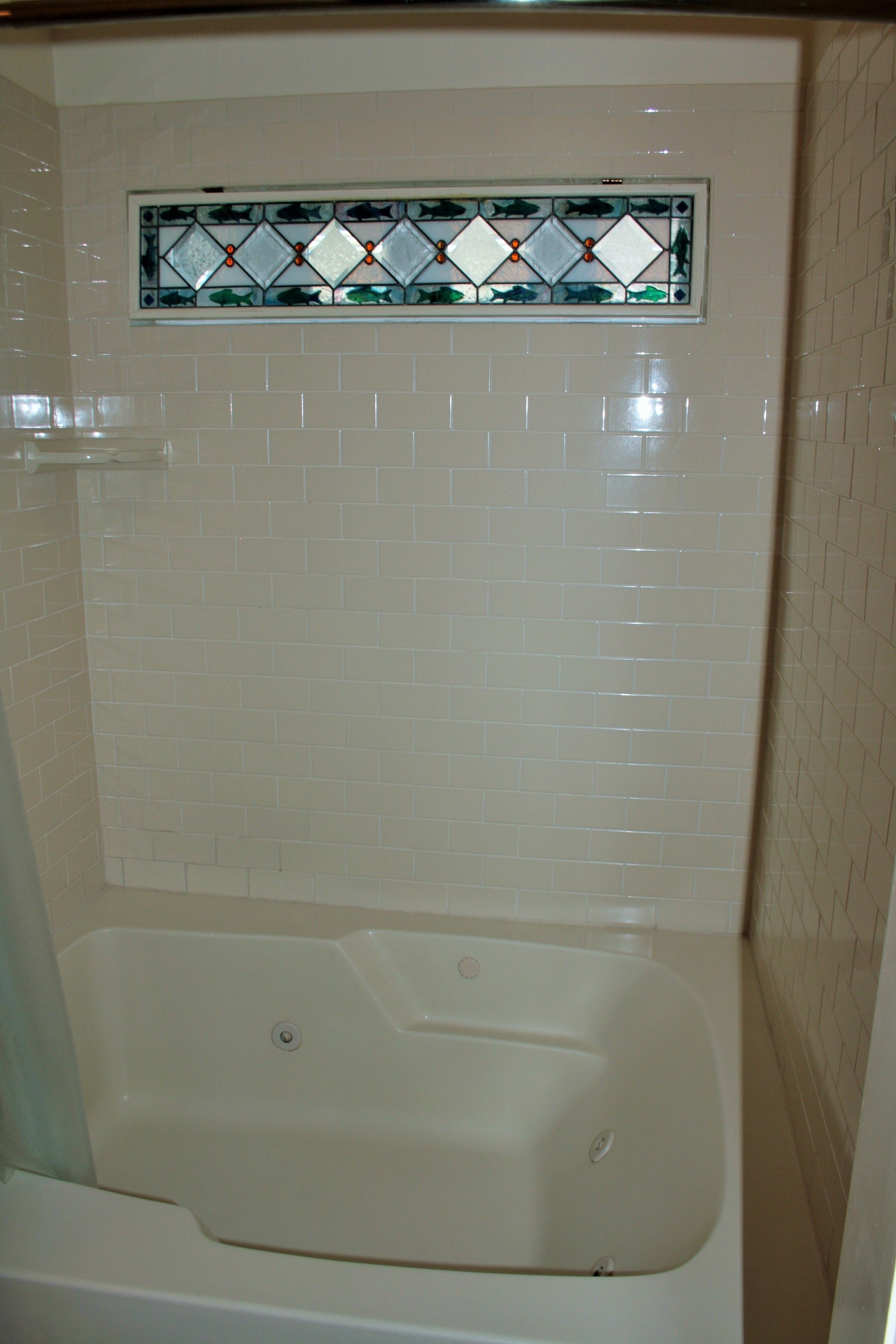 A bathroom with a bathtub, white tiled walls, and a stained glass window above the tub.