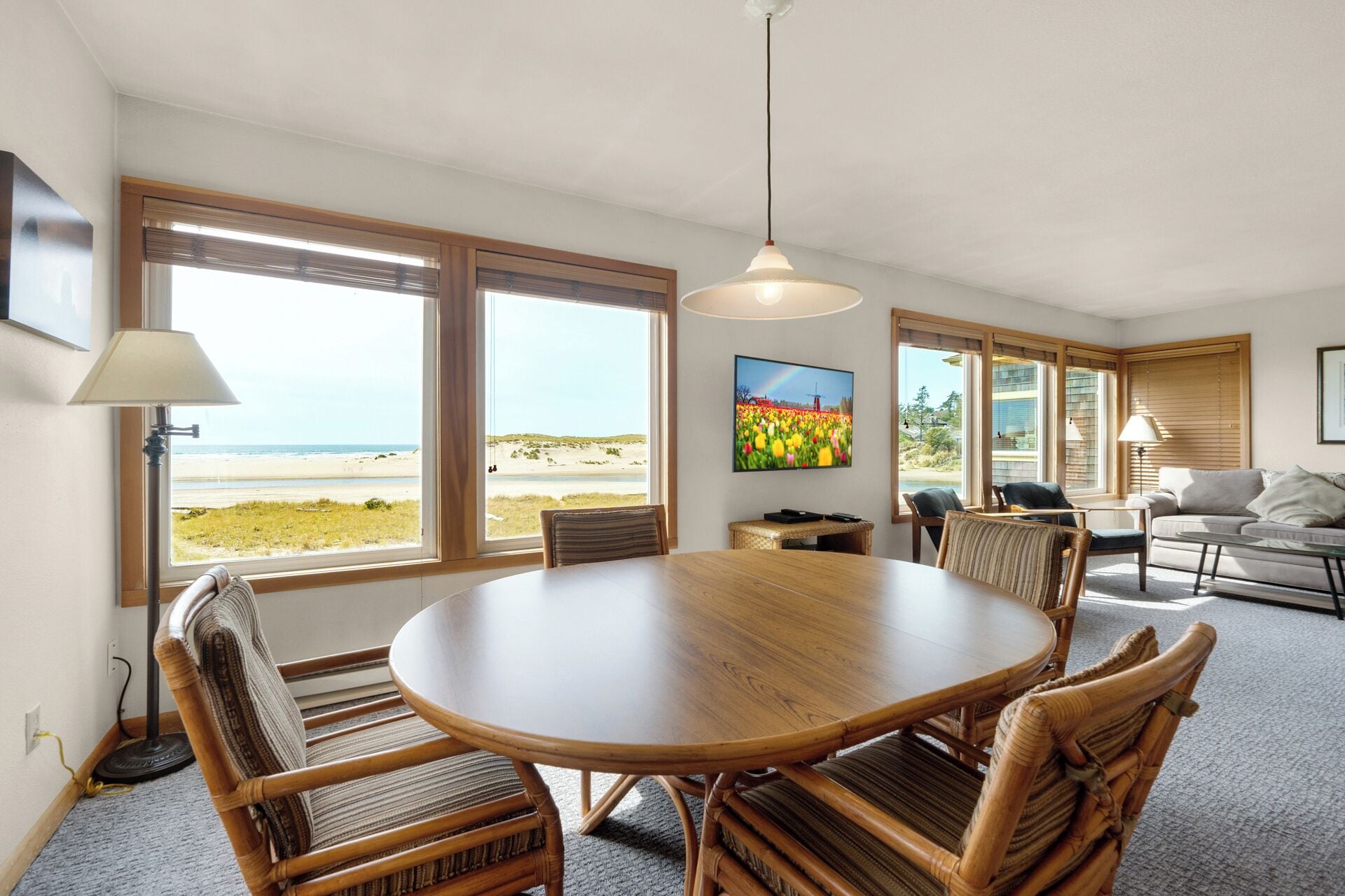 Une pièce spacieuse avec une grande table à manger en bois, entourée de chaises en osier, de grandes fenêtres donnant sur la plage et un coin salon confortable avec un canapé et des fauteuils.