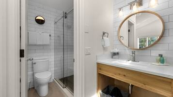 Un baño moderno con inodoro blanco, cabina de ducha de vidrio y tocador de madera con espejo.