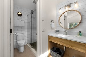 Un baño moderno con inodoro blanco, cabina de ducha de vidrio y tocador de madera con espejo.