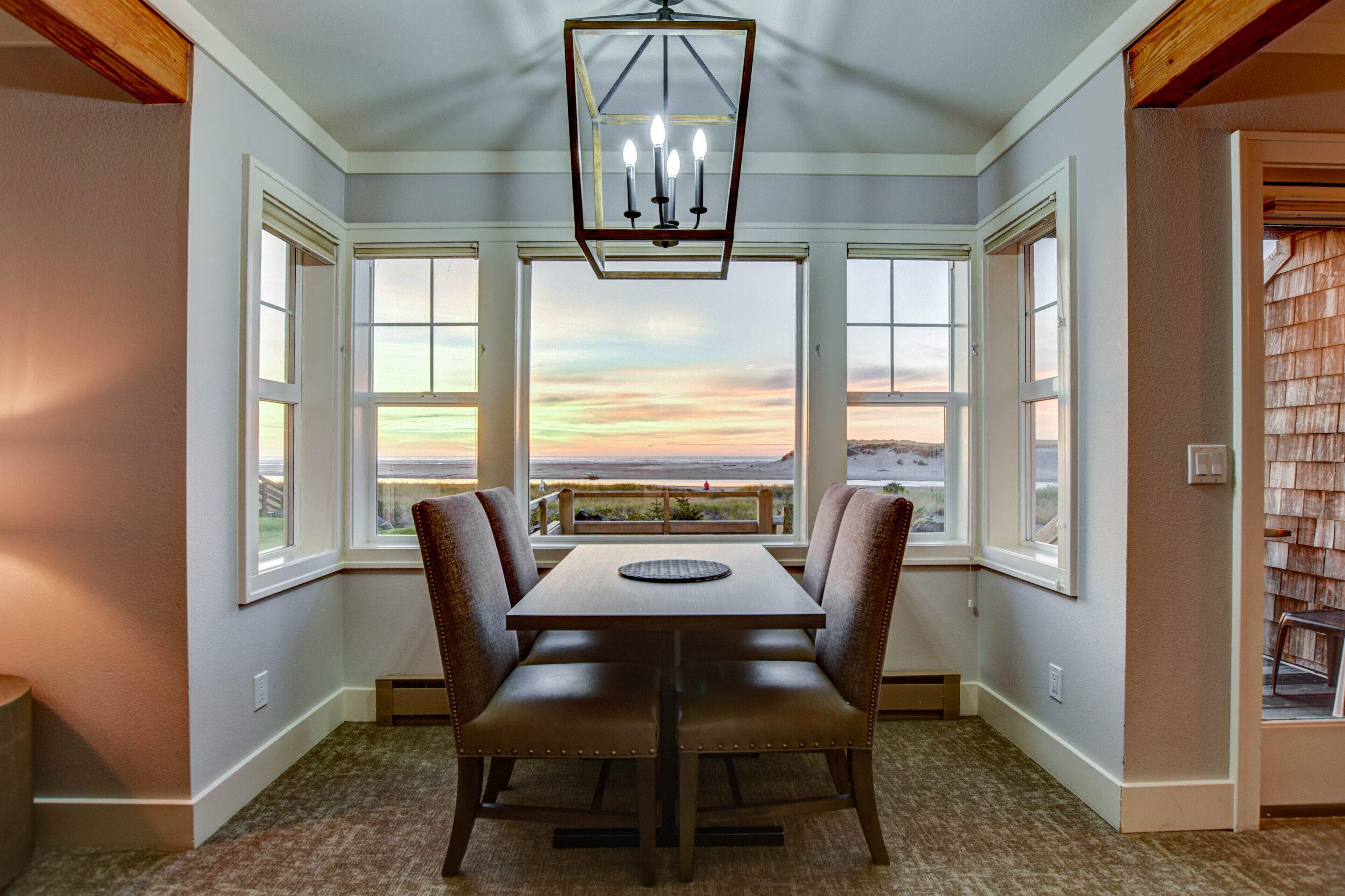 A dining area with a table and chairs, large windows with a view of the beach, and a chandelier.