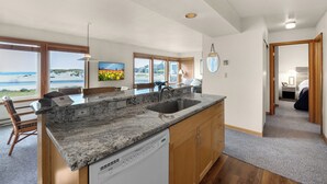 A spacious kitchen with a large island, a dishwasher, wooden cabinets, and a view of the beach.