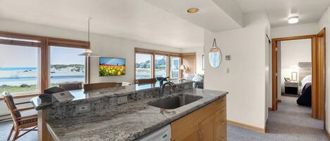 A spacious kitchen with a large island, a dishwasher, wooden cabinets, and a view of the beach.