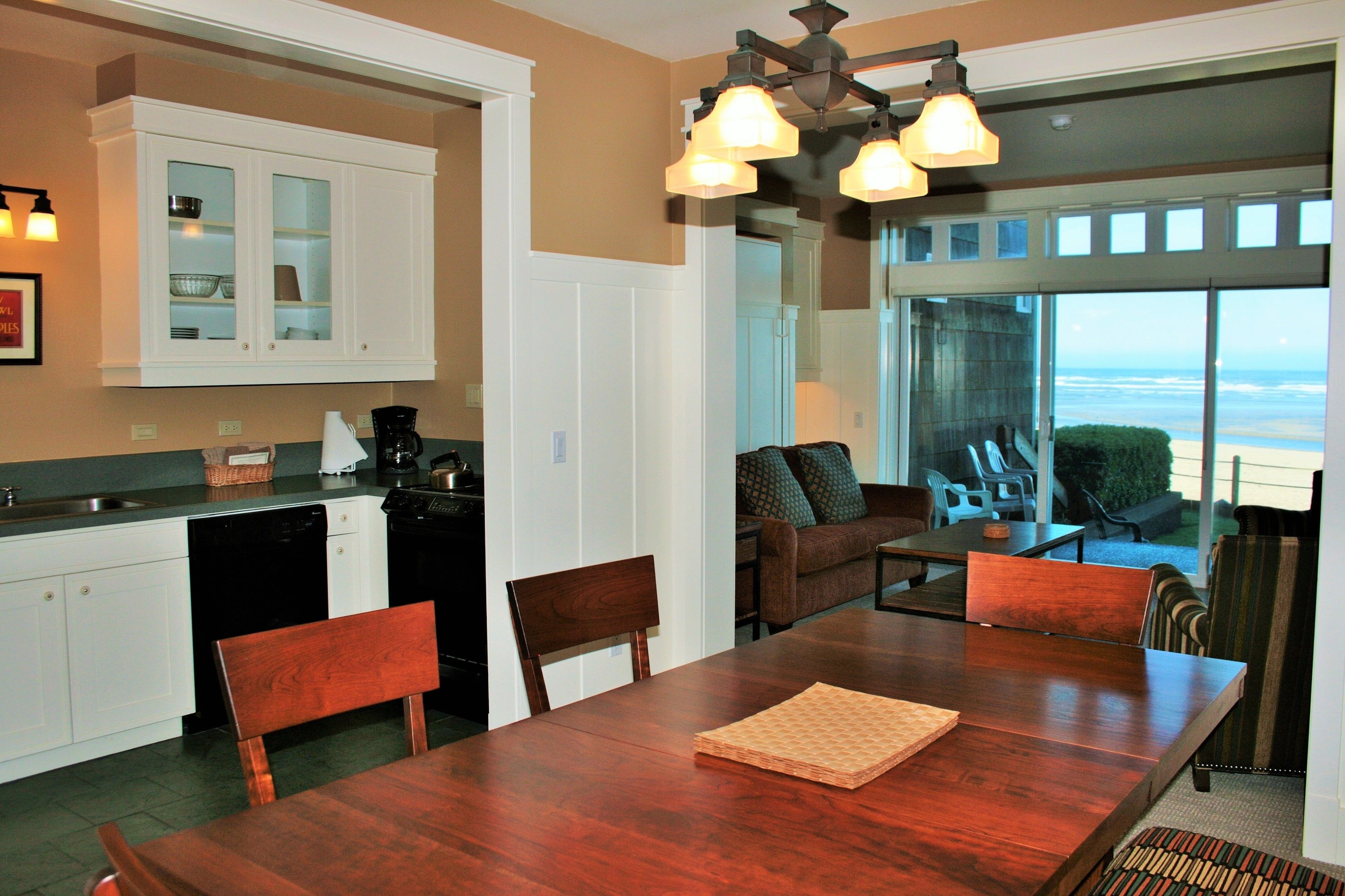 A kitchen with white cabinets, a dining table, and chairs. There is a view of the ocean through large windows.