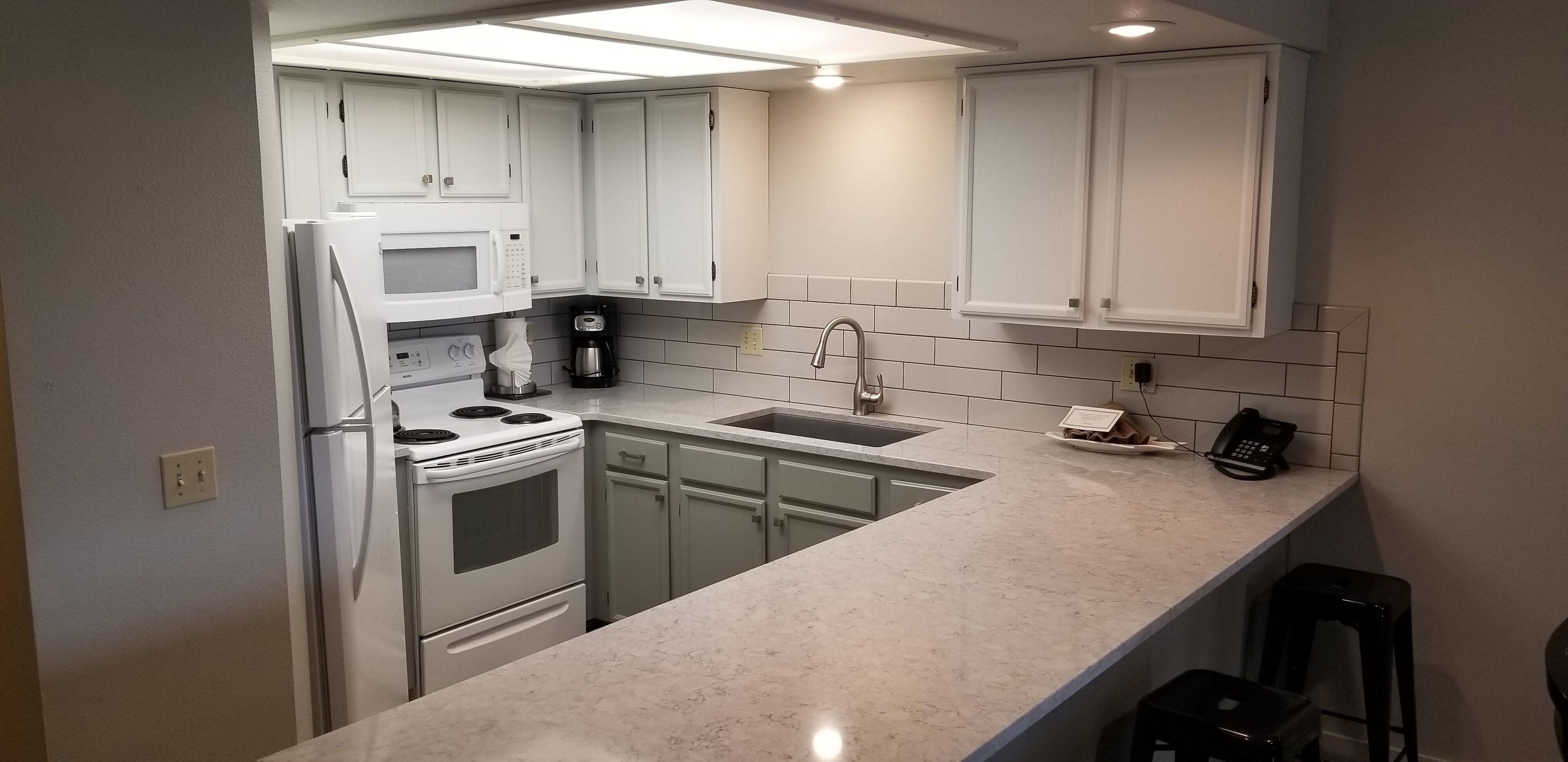 Una cocina moderna con armarios blancos, un refrigerador de acero inoxidable, un microondas, una cafetera y un fregadero.