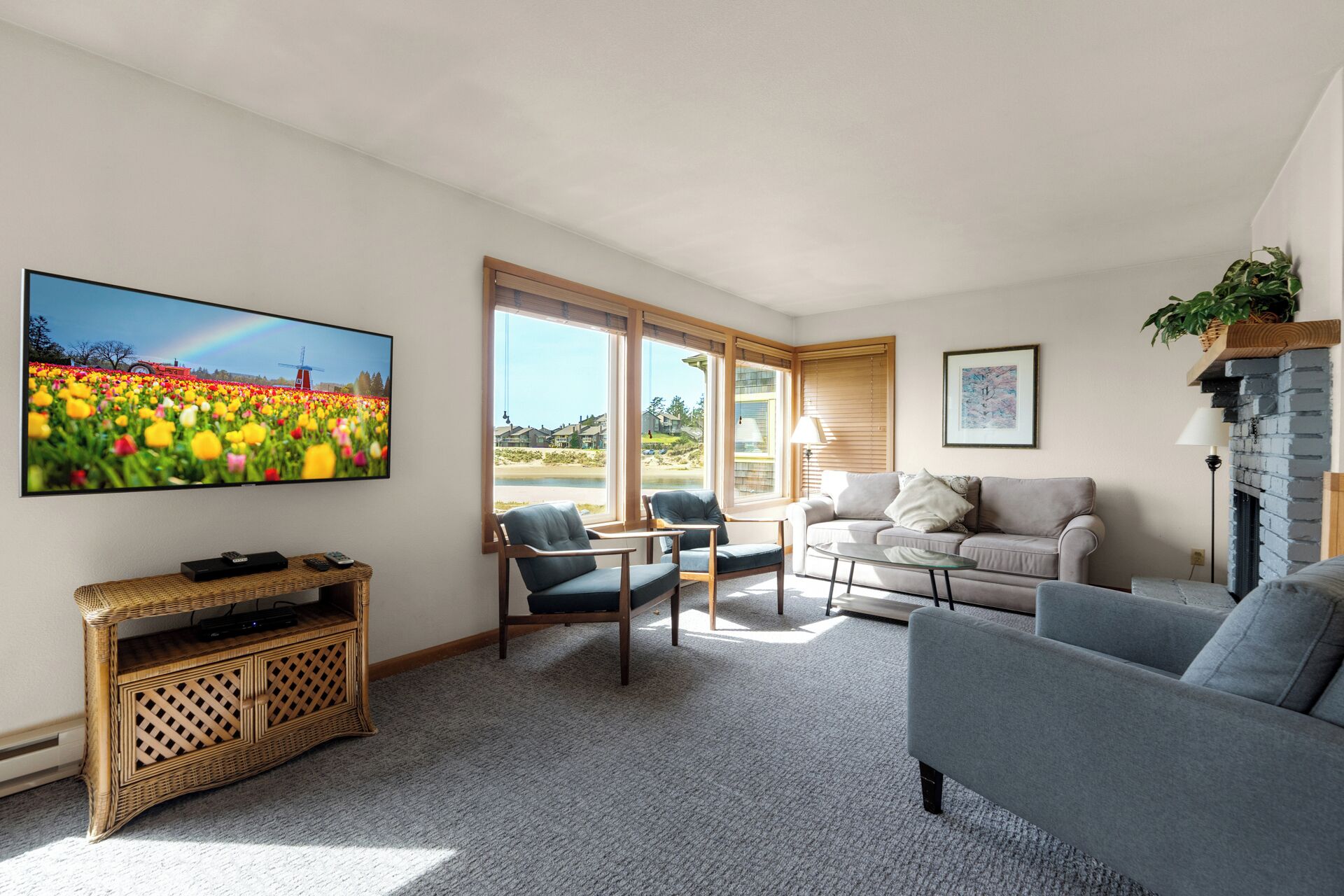 A living room with a large TV, wicker entertainment unit, grey sofas, and a fireplace.