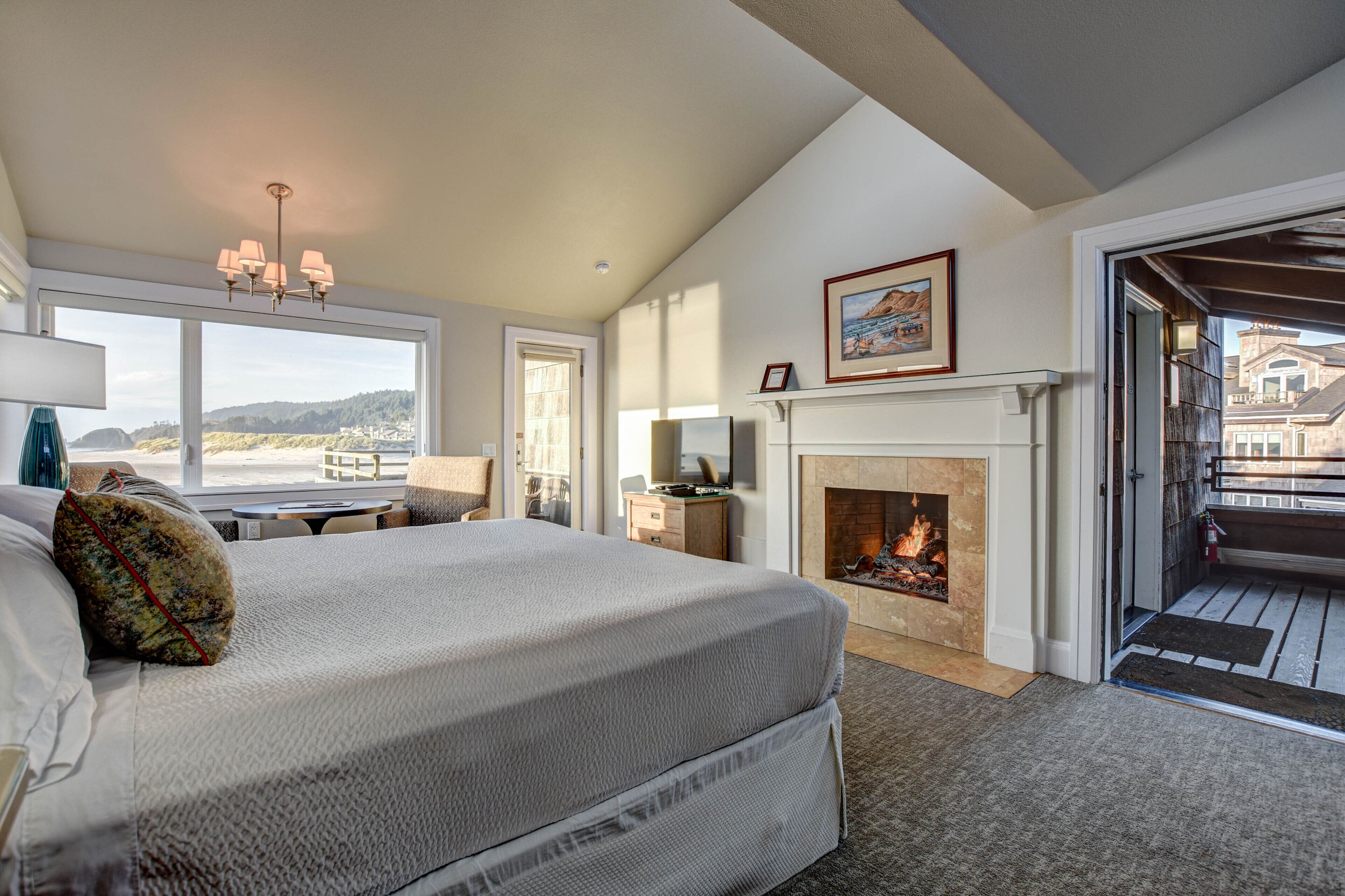 A bedroom with a large bed, a fireplace, a view of the outside, and a balcony.
