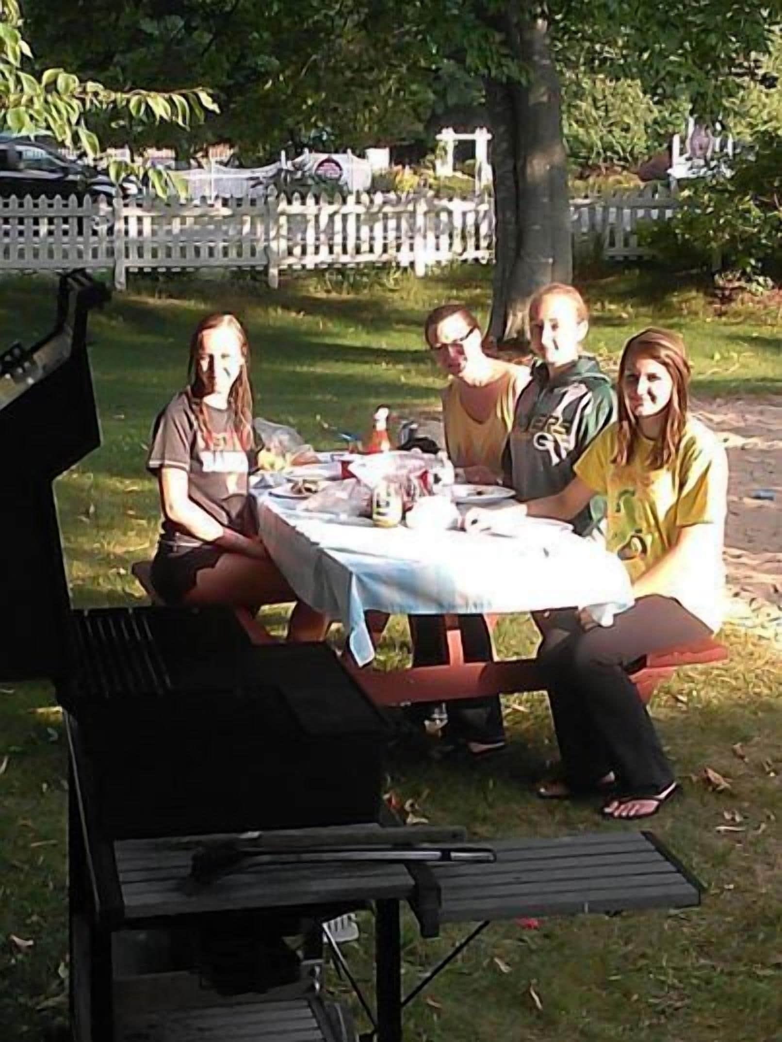 Un grupo de personas sentadas en una mesa al aire libre, con una parrilla al frente.