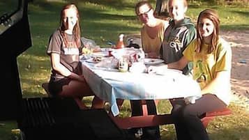 Un grupo de personas sentadas en una mesa al aire libre, con una parrilla al frente.