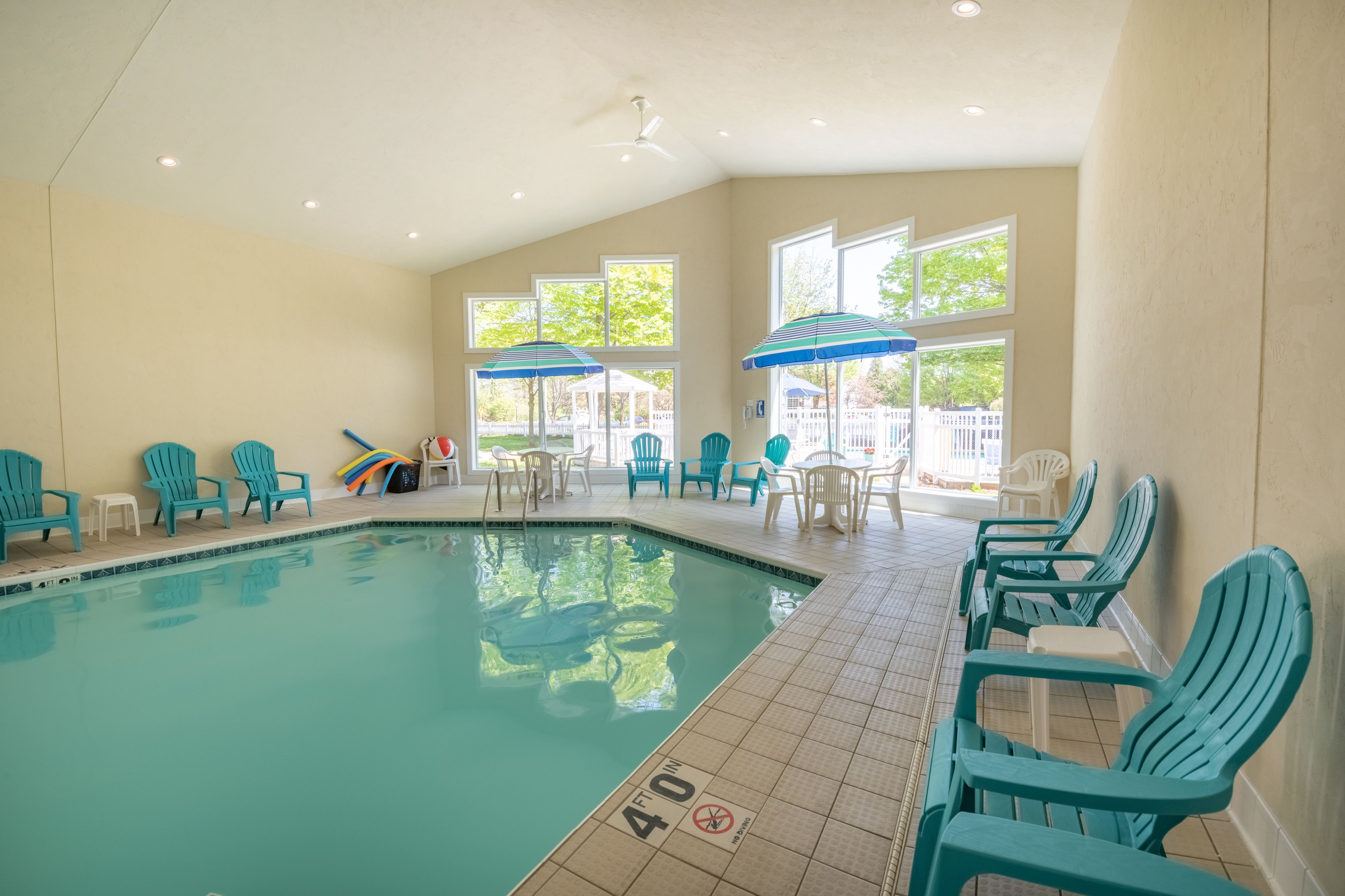 Ein Hallenbad mit blauen Stühlen, Sonnenschirmen, einem Deckenventilator und großen Fenstern.