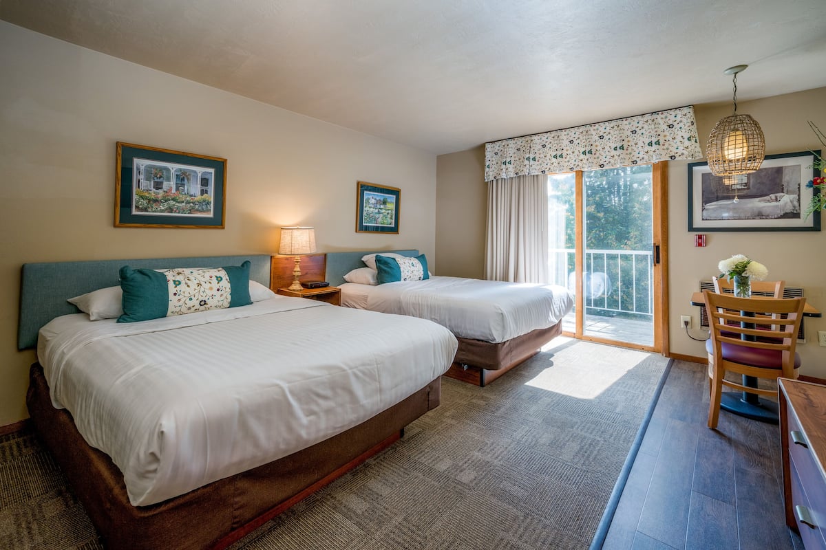 Quarto de hotel com duas camas, uma mesa de jantar e vista para o exterior.