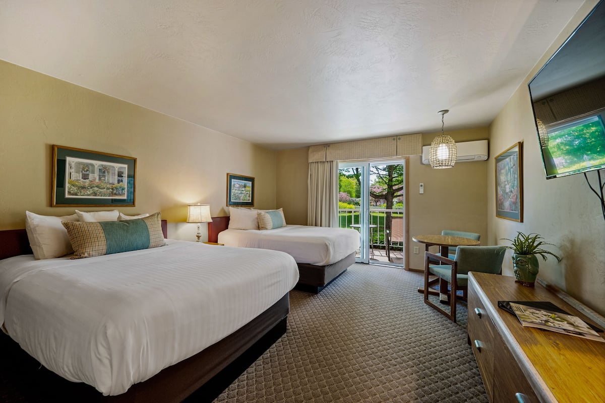 Quarto de hotel com duas camas, uma escrivaninha, uma cadeira, televisão e varanda com vista para árvores.