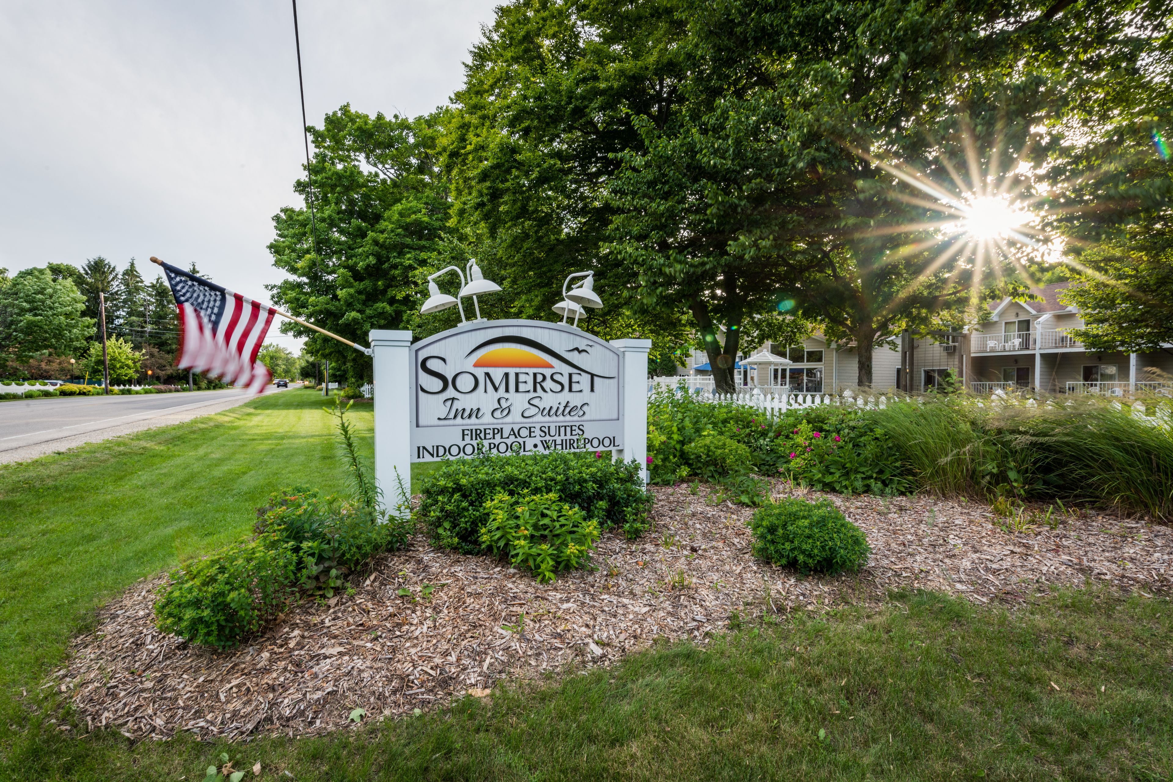 Señal de Somerset Inn & Suites con una bandera, árboles y una valla de fondo.
