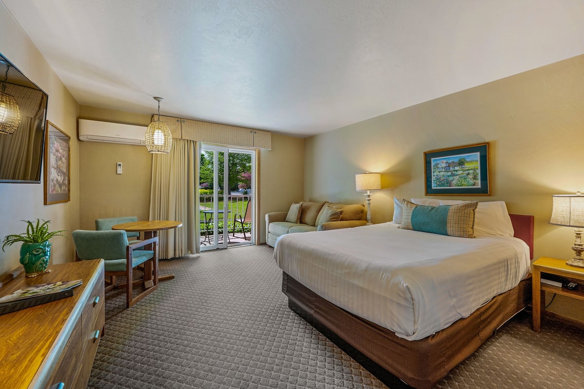 Quarto de hotel com cama, escrivaninha, cadeira, mesa, sofá e janela com vista para o verde.