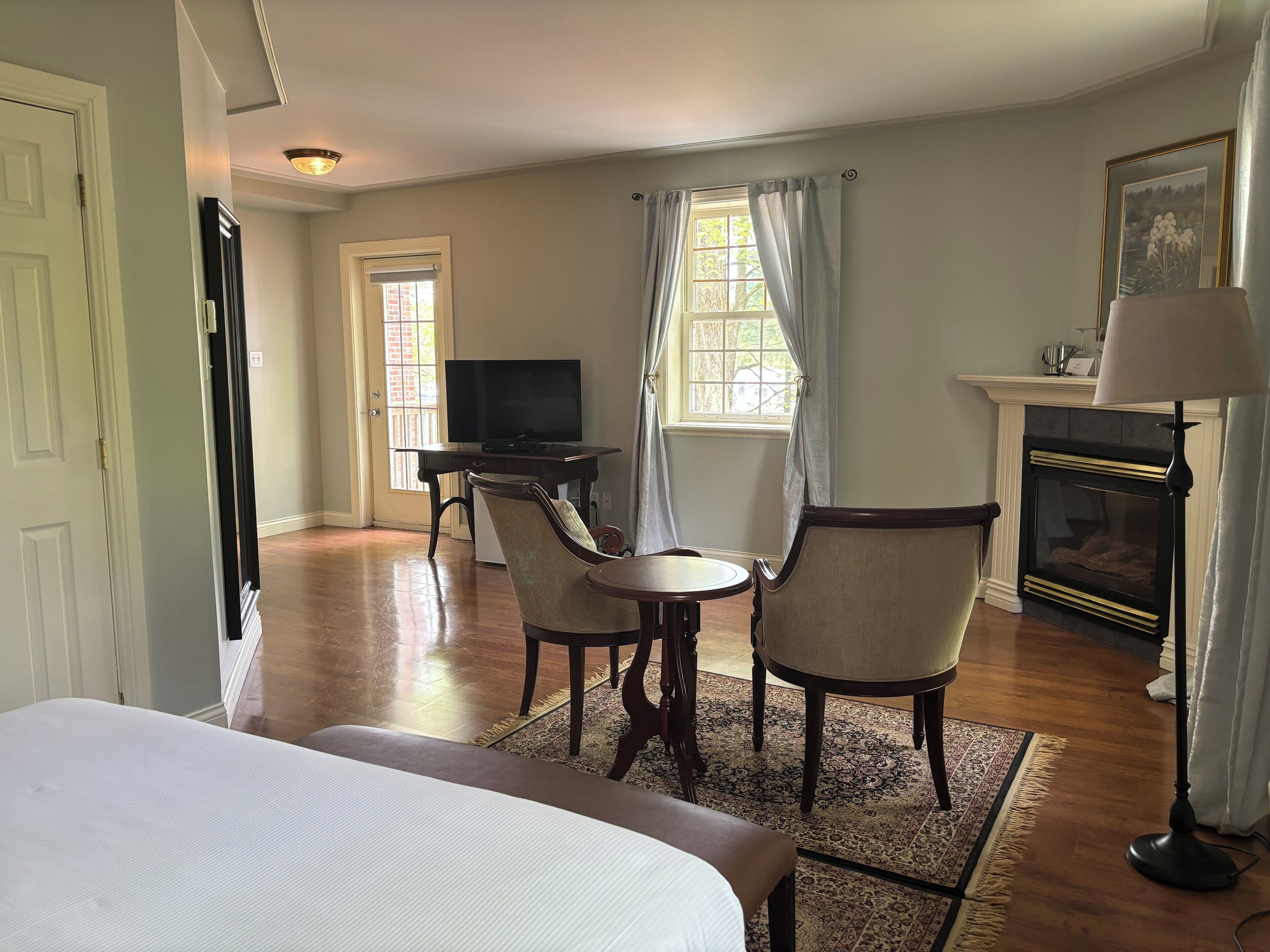 Une chambre d’hôtel avec un lit, un bureau avec une télévision, une cheminée et une fenêtre avec des rideaux.