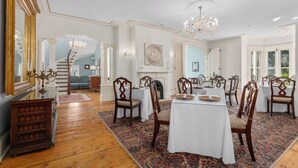 A formal dining room with a chandelier, wooden chairs, and a white tablecloth. - Manoir Sweetsburg (Cowansville)