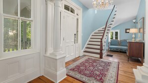 A spacious hallway with a wooden staircase, a large window, and a chandelier. - Manoir Sweetsburg (Cowansville)