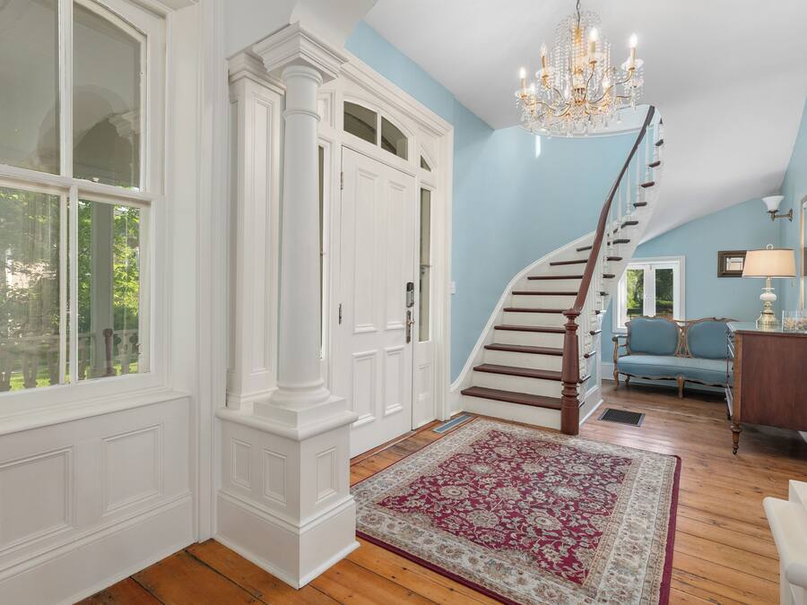 A spacious hallway with a wooden staircase, a large window, and a chandelier.