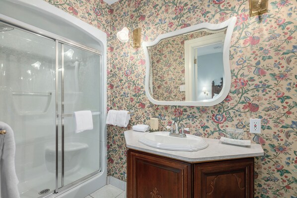A bathroom with a shower, a sink with a mirror, and floral wallpaper. - Manoir Sweetsburg (Cowansville)