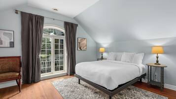 Een slaapkamer met een groot bed, twee nachtkastjes met lampen, een stoel en een raam met gordijnen.