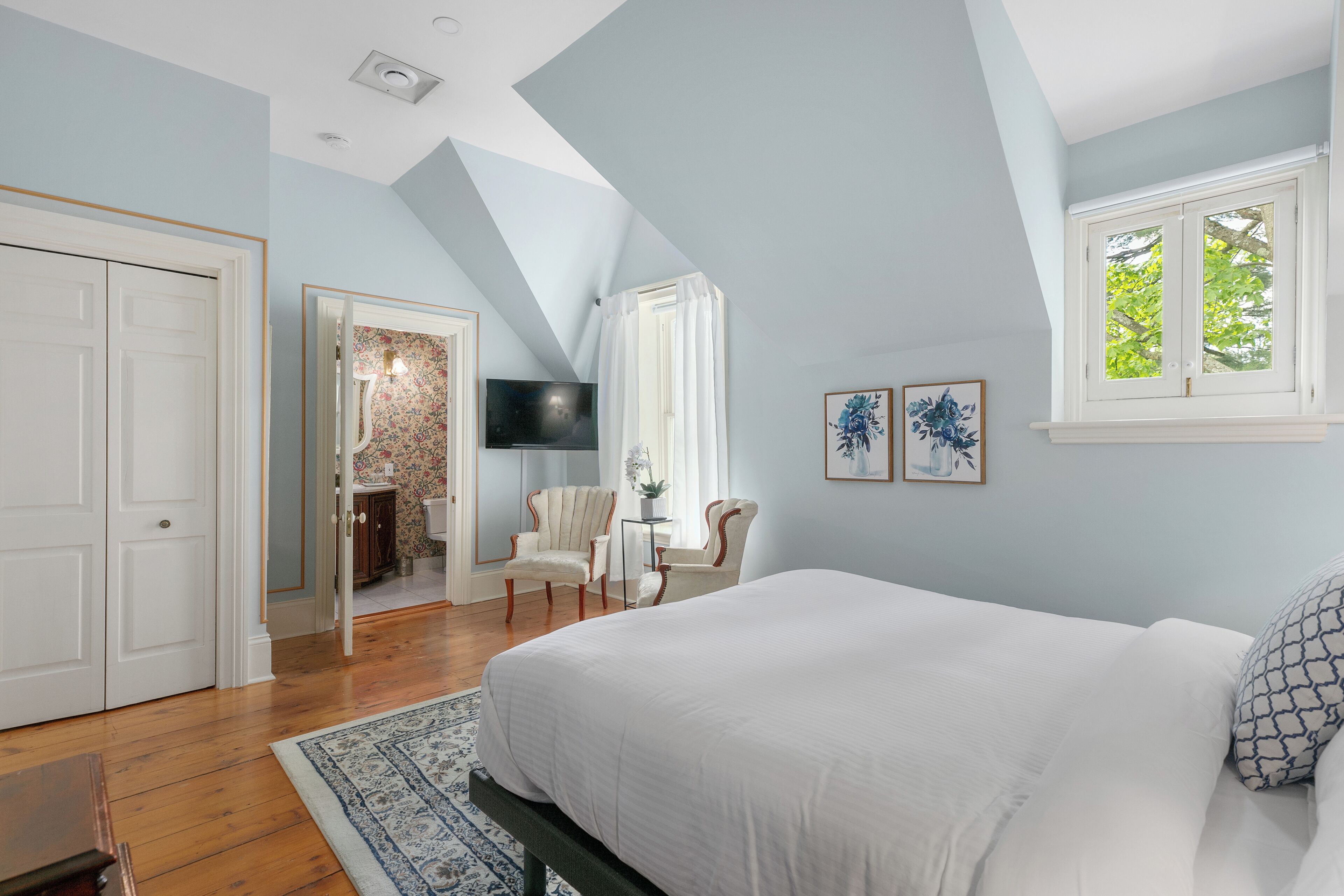 A bedroom with a large bed, a TV, a chair, and a window with curtains.