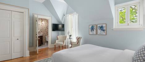 A bedroom with a large bed, a TV, a chair, and a window with curtains.