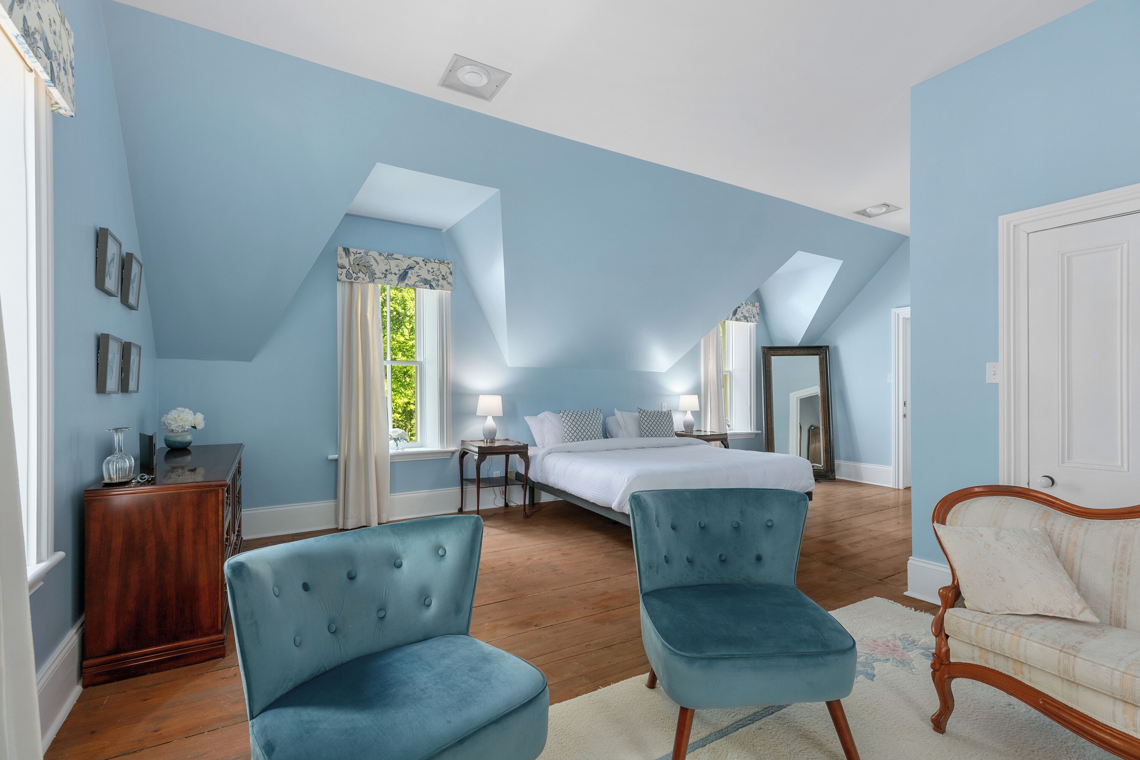 Une chambre à coucher avec un lit, deux chaises, une commode et un miroir.