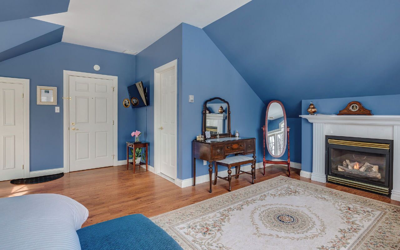 Um quarto com uma cama grande, cômoda, espelho, lareira e parede azul.