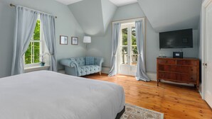 A bedroom with a large bed, a wooden dresser, a television, and a balcony with curtains. - Manoir Sweetsburg (Cowansville)